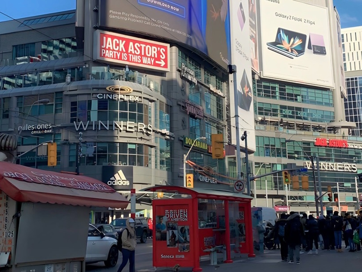 Glass buildings and billboards with pedestrians walking on the street.