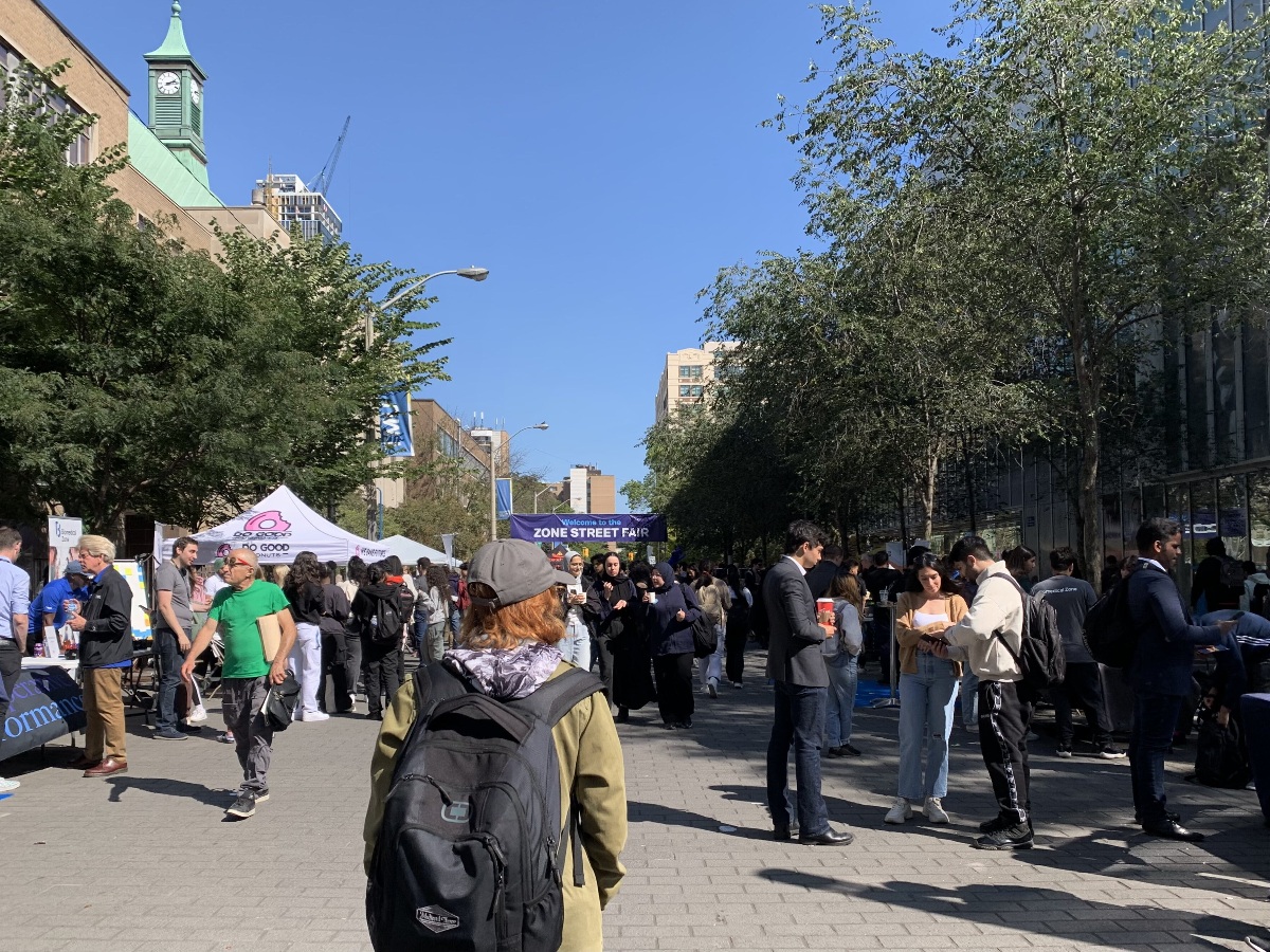 Students surround a street with a banner that says "Zone Street Fair." 