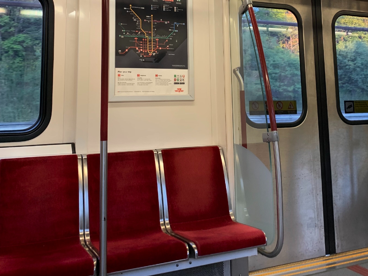 Inside of a subway cart with trees outside of the windows.