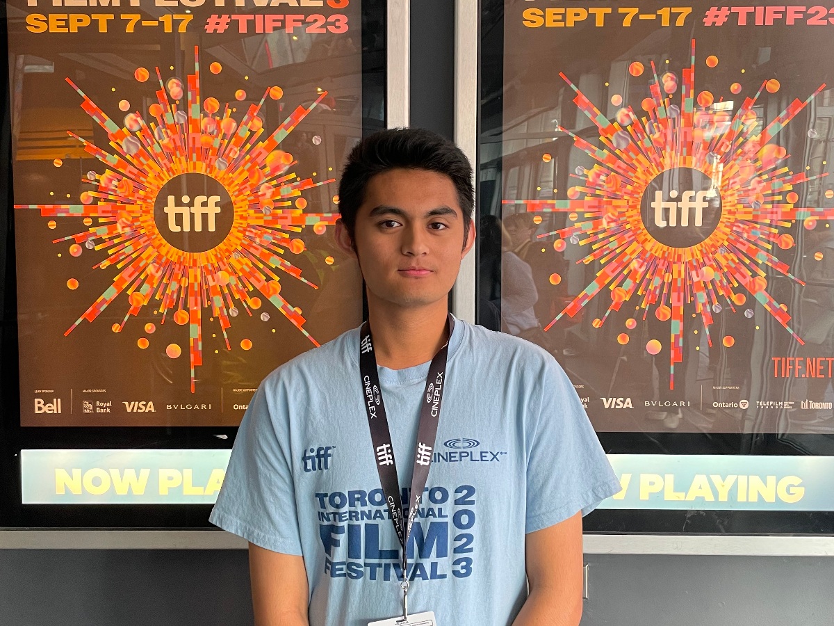 Jack is standing in front of two posters that say TIFF on it. He is wearing a shirt that says "Toronto International Film Festival 2023". 