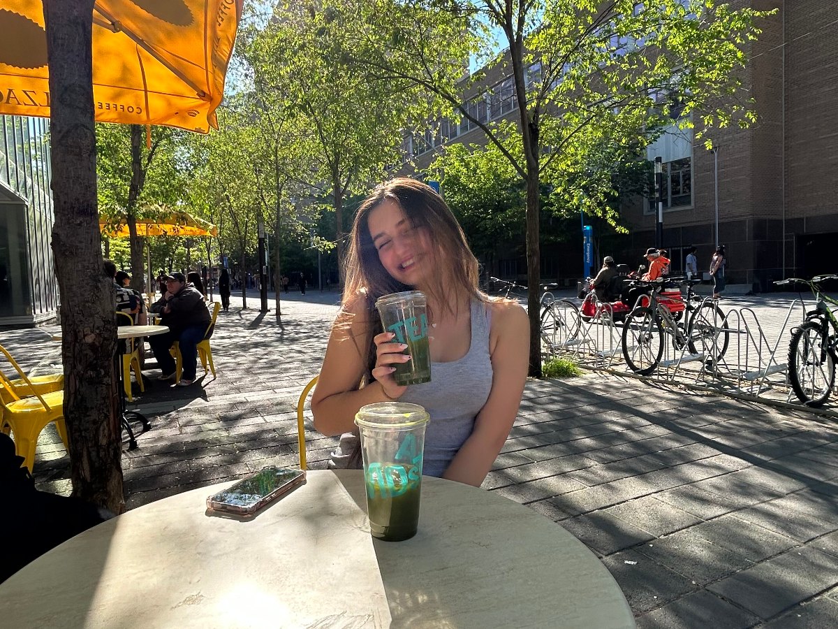 Mila is at a coffee shop named Balzac's and holding a cup with a green drink inside.