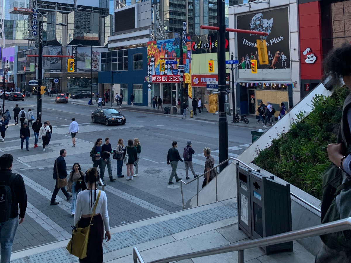 View from the TMU campus of vibrant coloured restaurants and clothing stores on Yonge Street, while students walk down it.