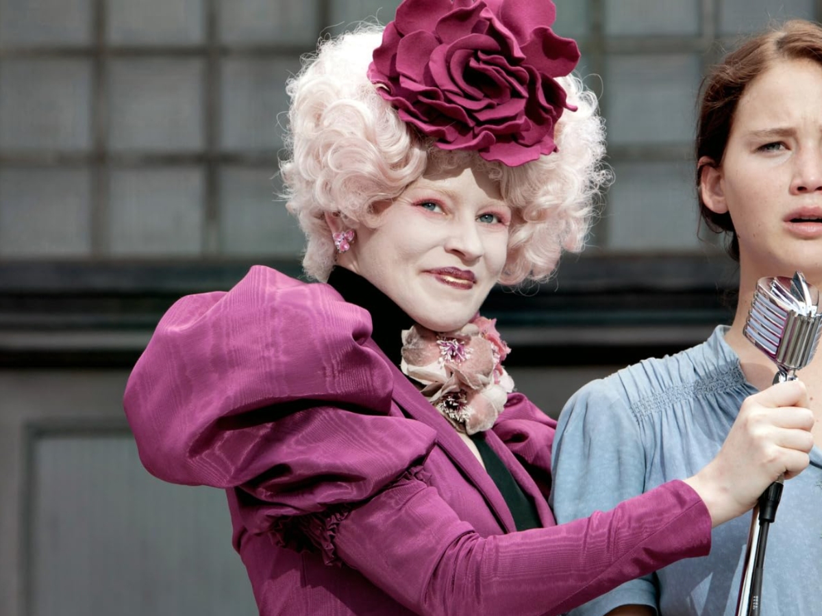 Effie smirks in her big curly hair and puffy shirt while holding a microphone.
