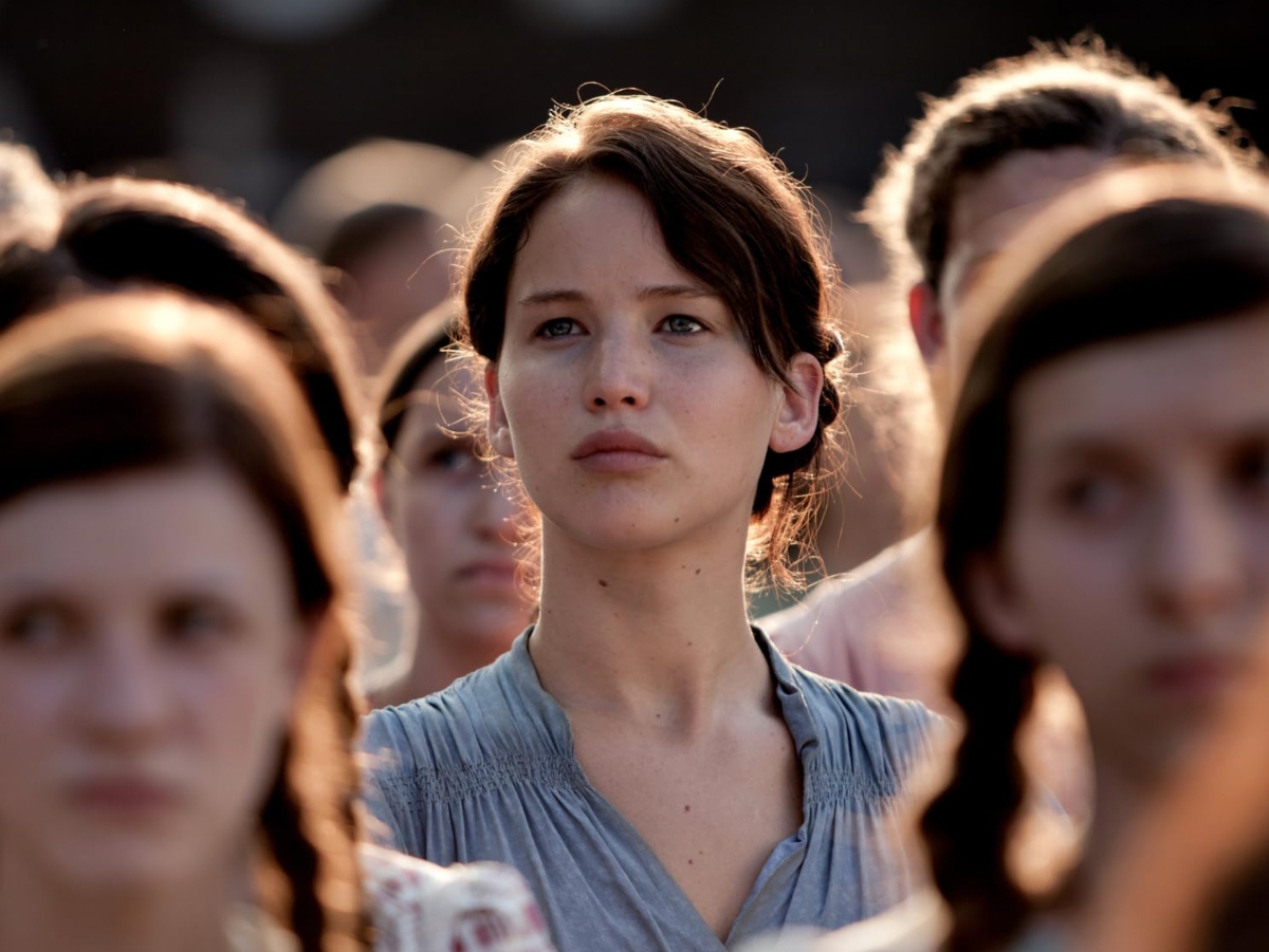 Katniss stares straight ahead of the crowd with a solemn expression.