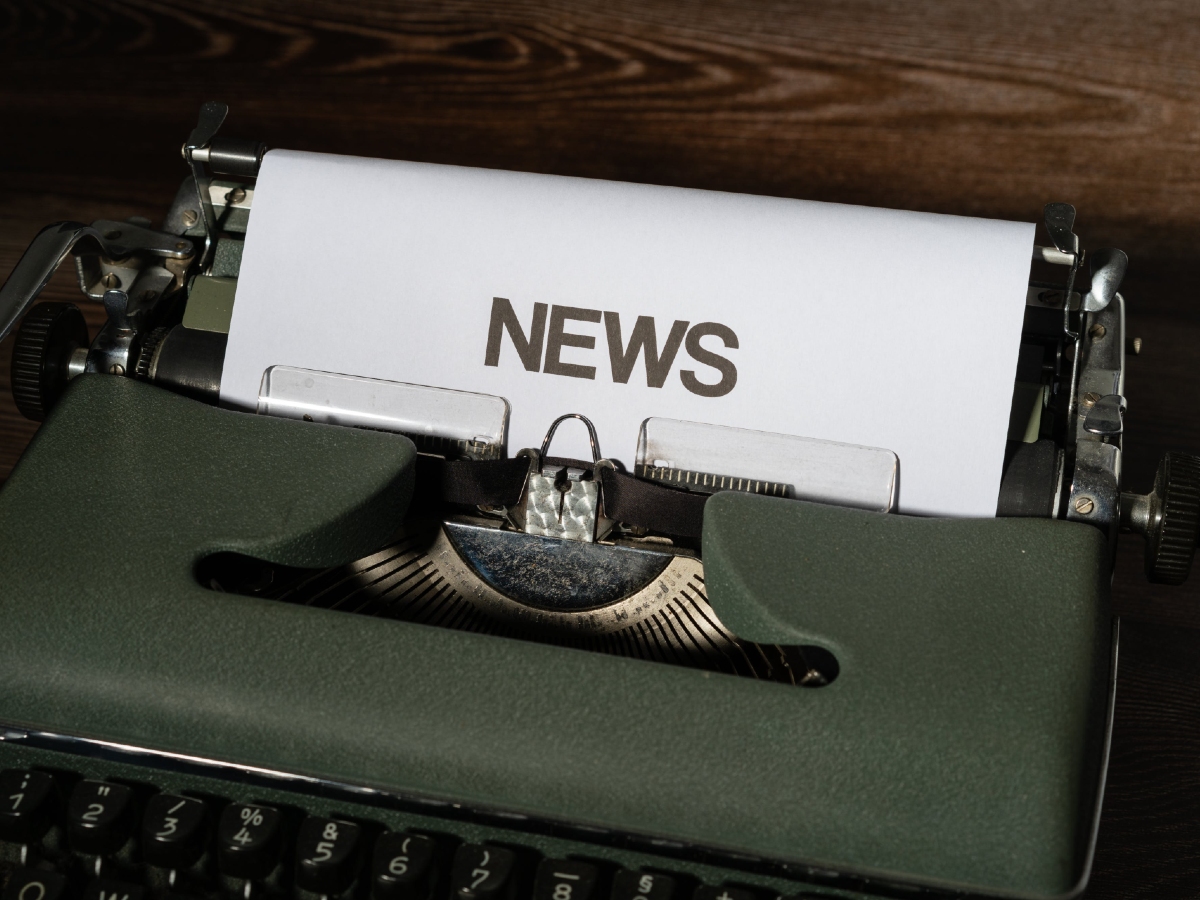 With dim ambience, a dark green typewriter has a paper attached to it with the word "news" on it.