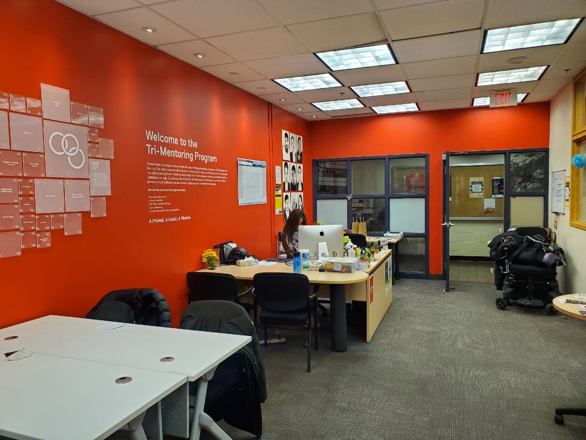 The Tri-Mentoring Program office has bright red walls with posters on it and tables against it.