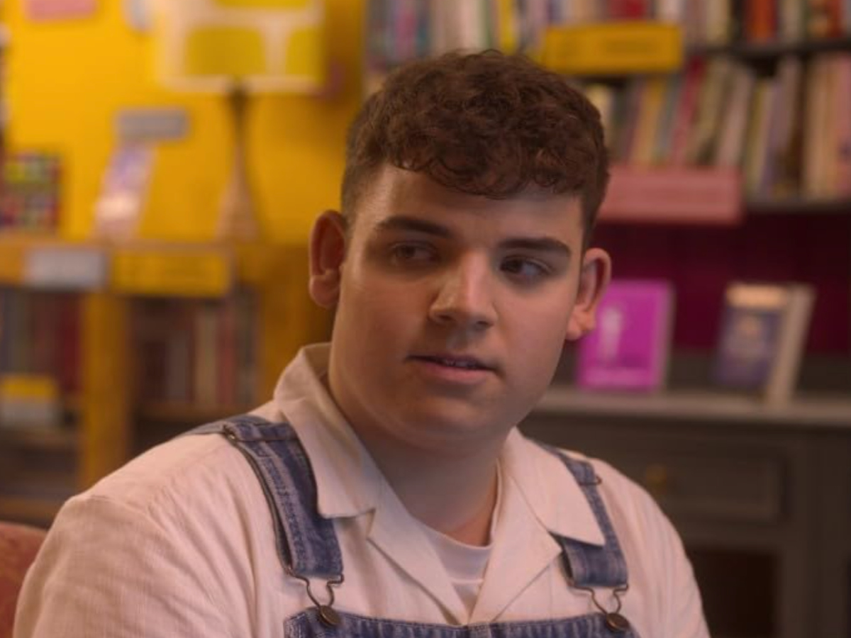 Isaac faces his friend while sitting in a bookshop