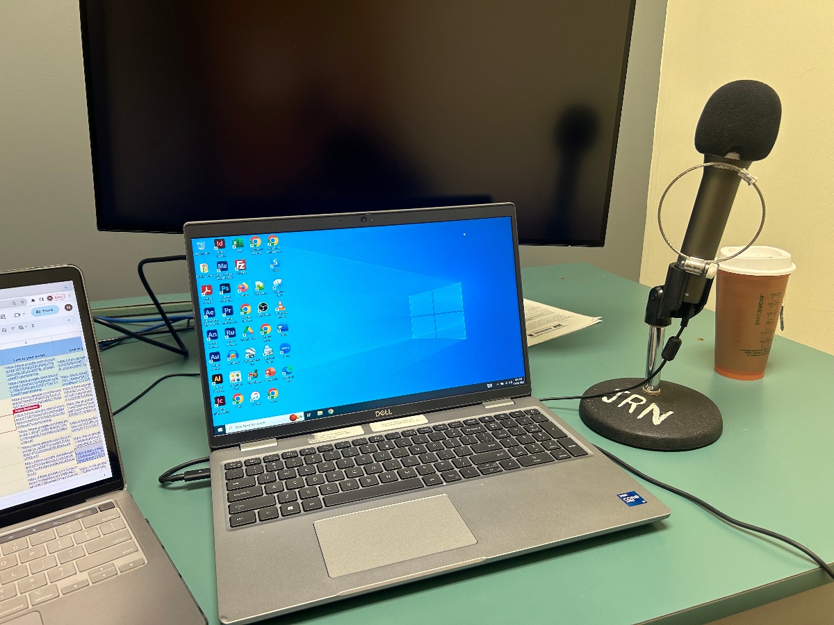 Computer screens and a microphone with JRN written on it sit on a table.