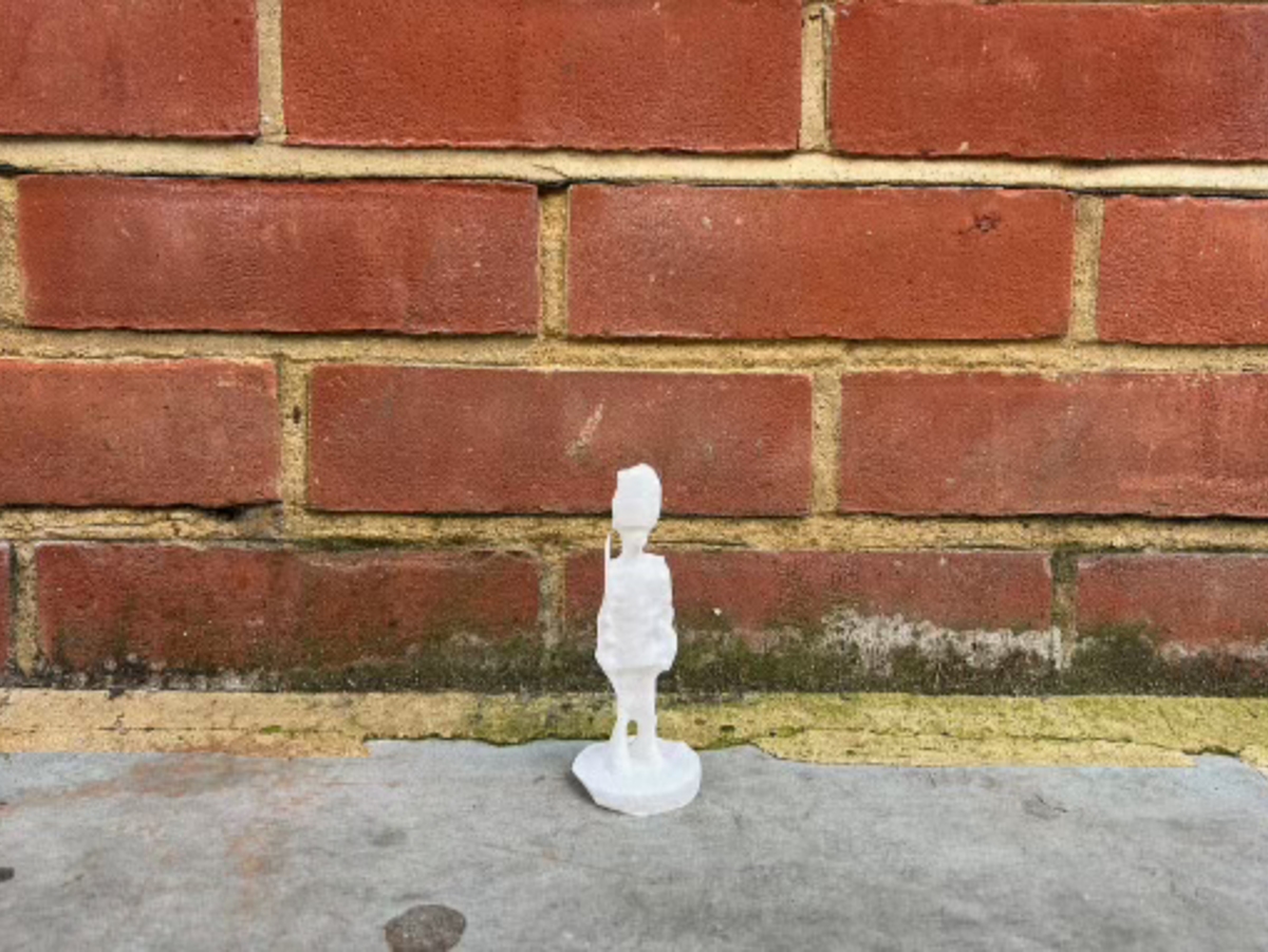 A warm and grainy ambiance captures a 3D-printed London guard figurine standing in front of a brick wall.