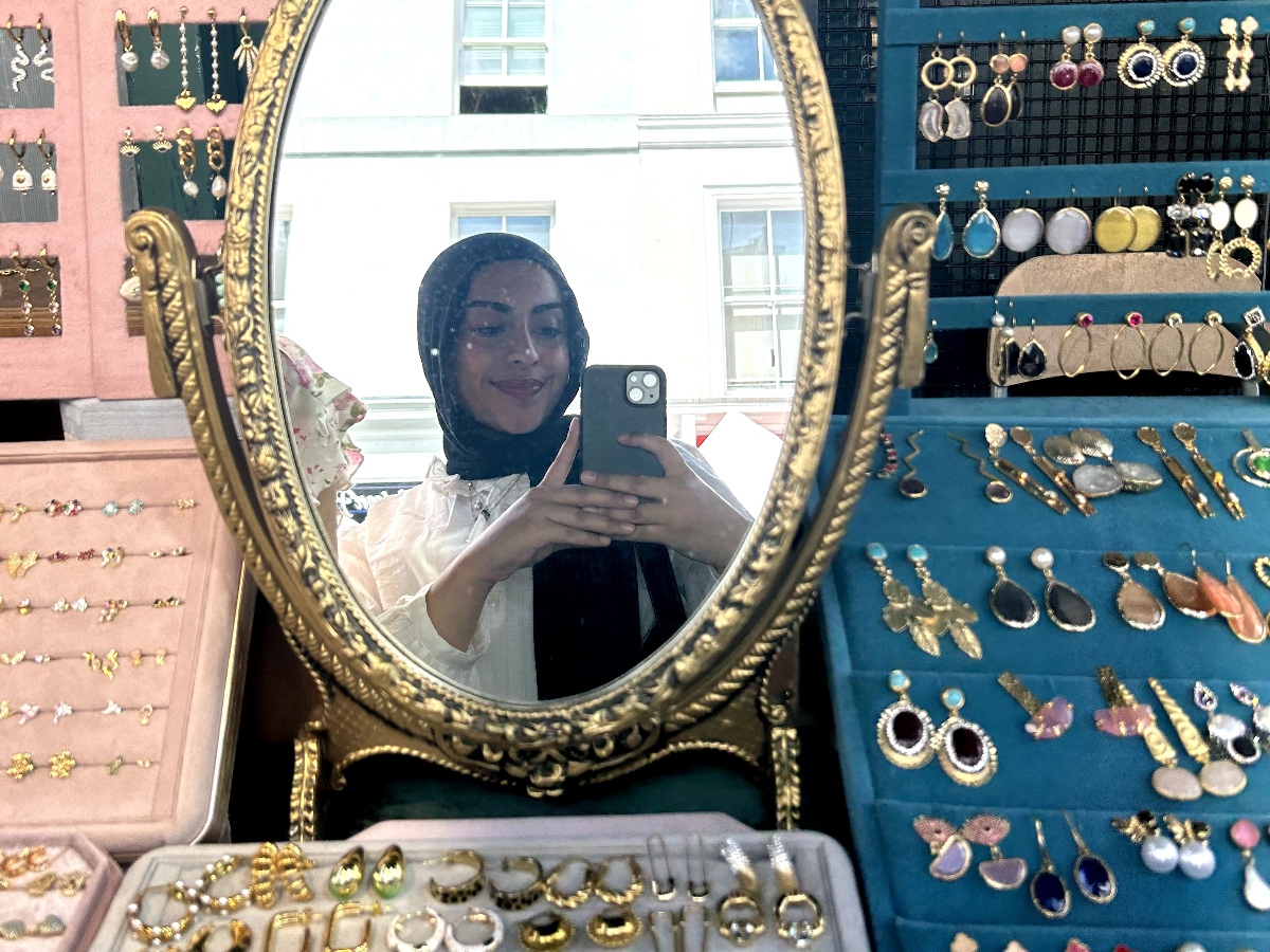 Hadiqah smiles in the mirror of a vintage jewellery booth in Notting Hill.