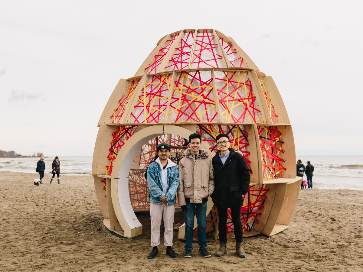 A colourful dome-shaped sculpture stands behind Henry and his teammates on a cloudy day at the beach.