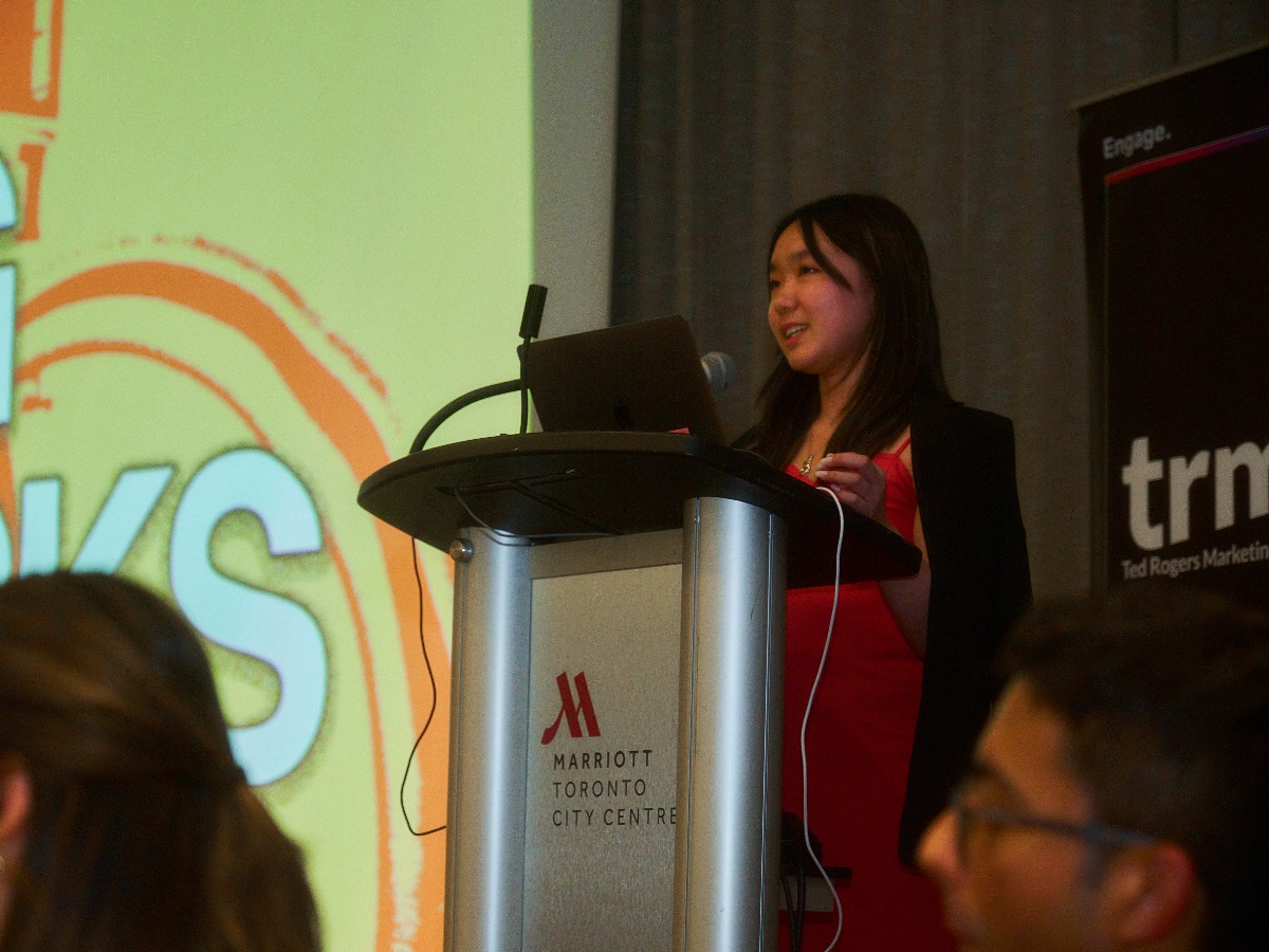 Shannon stands behind a podium and speaks to the audience at the Marriott Toronto City Centre.