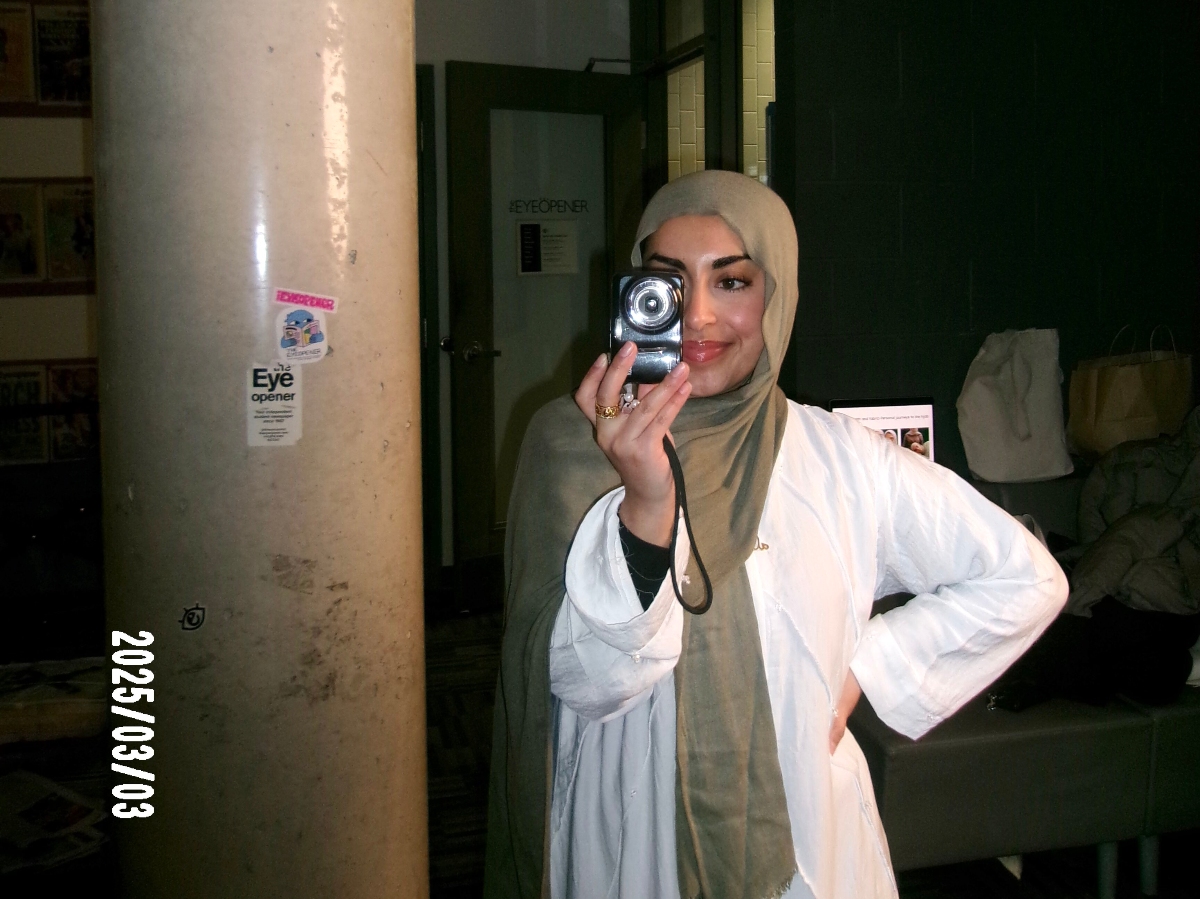 Hadiqah holds a digital camera up to her face in The Eyeopener office.