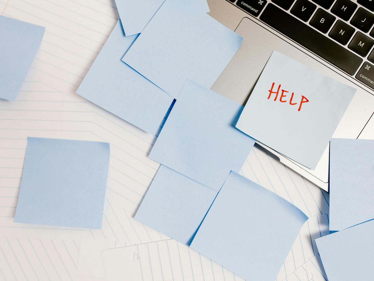 A collection of blank sticky notes on a stack of lined paper and laptop keyboard with the word "help" written on one of them. 