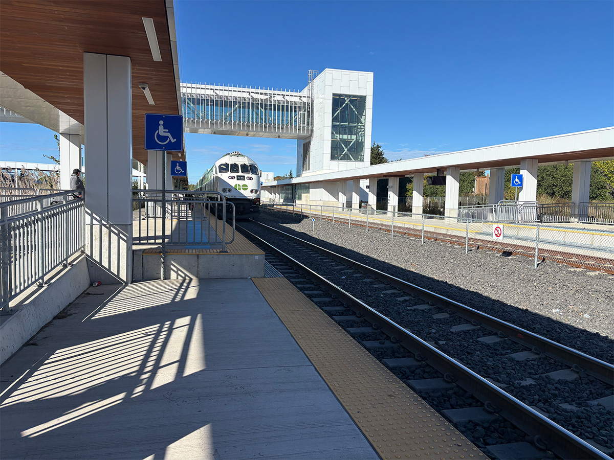A GO train arrives at an exterior train platform on a bright, sunny day.