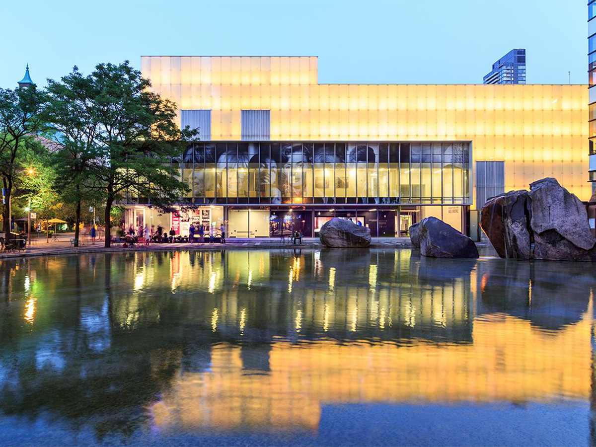 The illuminated exterior wall of the Image Arts Centre at dusk, reflected in TMU's campus pond, Lake Devo.