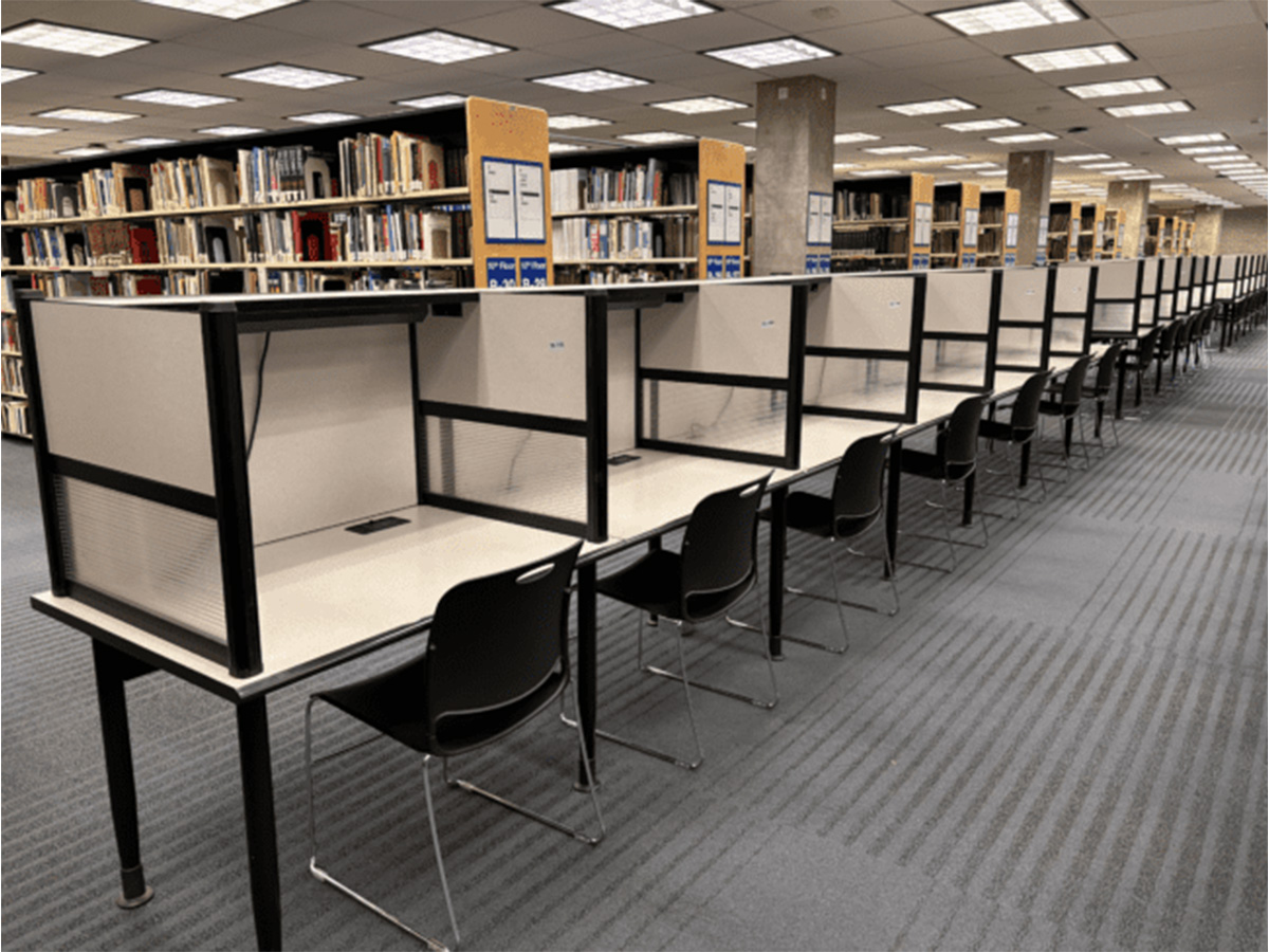 A row of individual study carrels at the TMU Library in the middle of several filled book shelves.