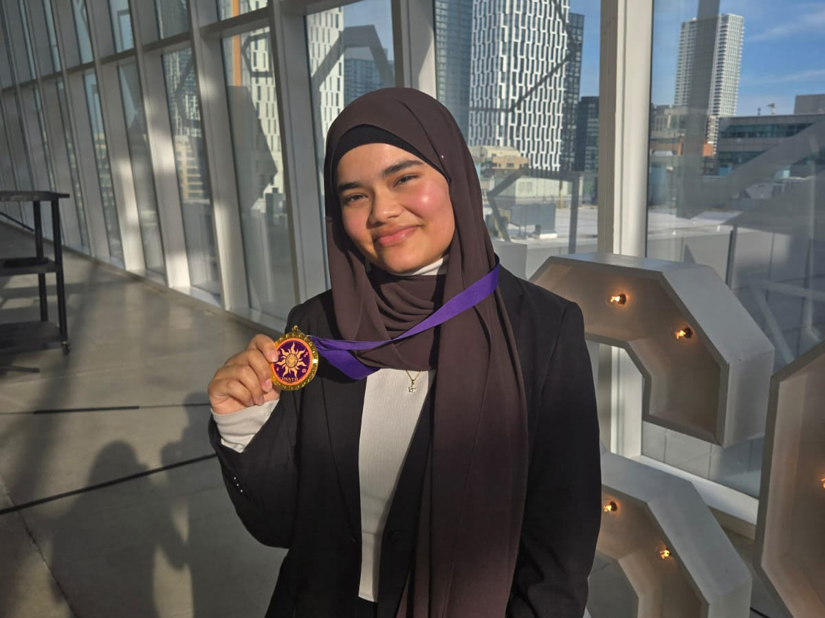 Umayyah poses on the 8th floor of the Student Learning Centre (SLC) and shows off a medal..