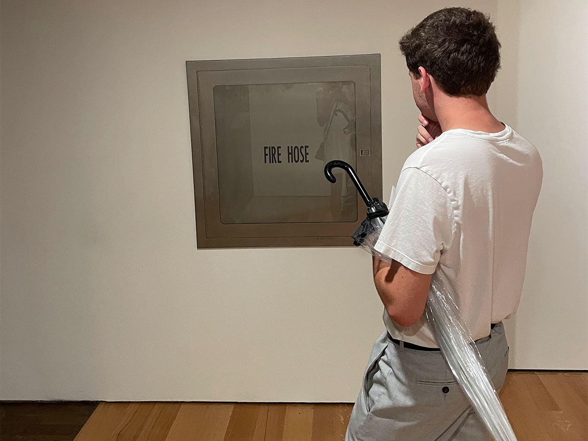 Ido stares at a fire hose cabinet in the wall of a gallery, pretending to admire it as an art piece.