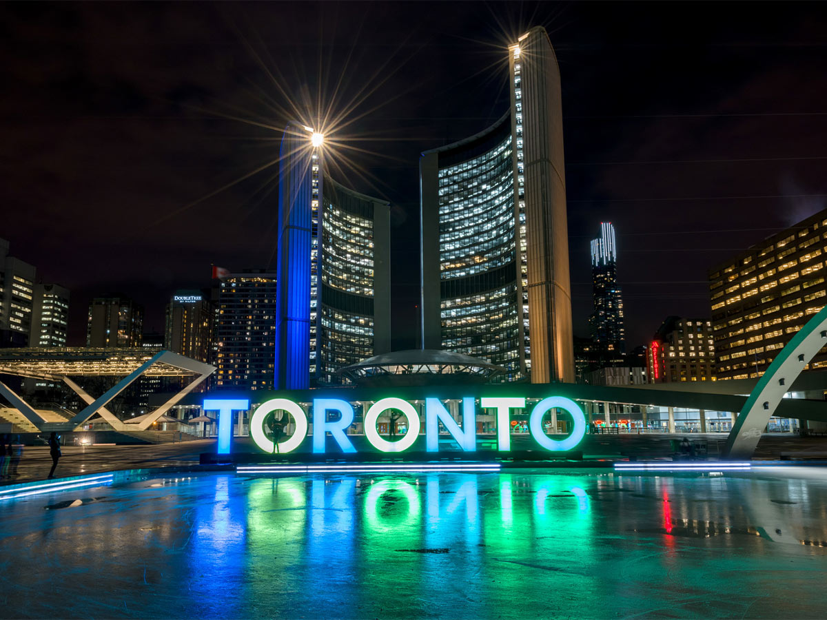In front of City Hall, the bright Toronto sign illuminates the frozen ice rink of Nathan Phillips Square in the dark.