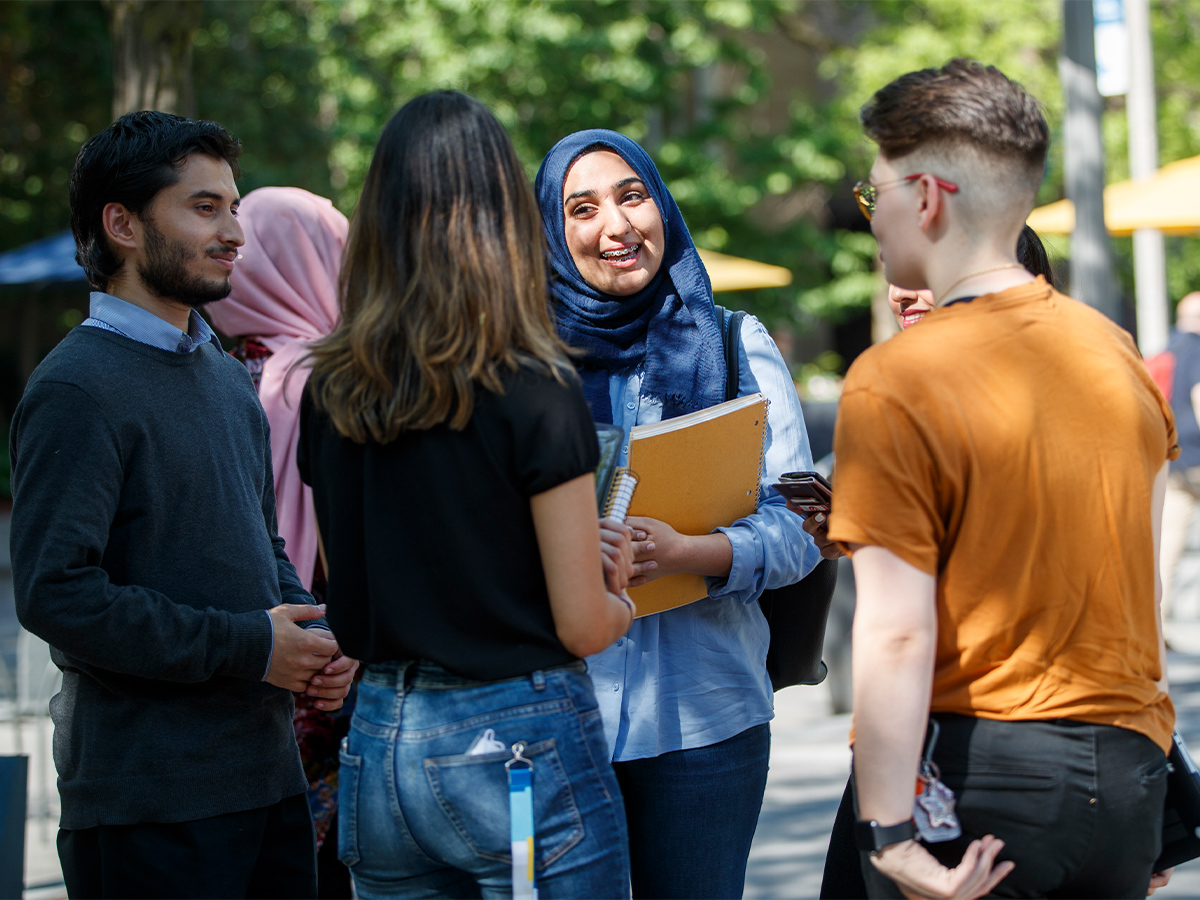 A group of smiling friends chat on Gould Street on a sunny day.