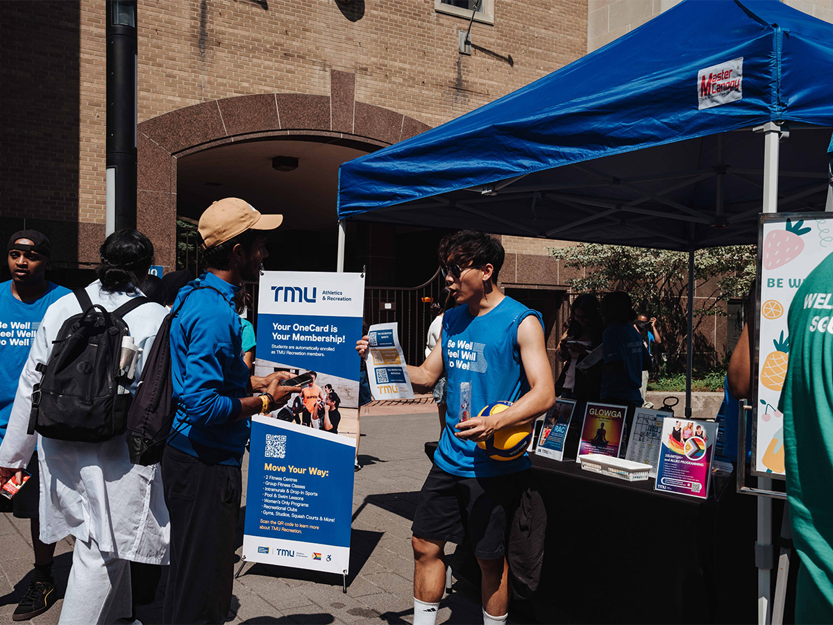 At a booth on Gould Street during Orientation, a student representing Athletics & Recreation provides information to a new TMU student.