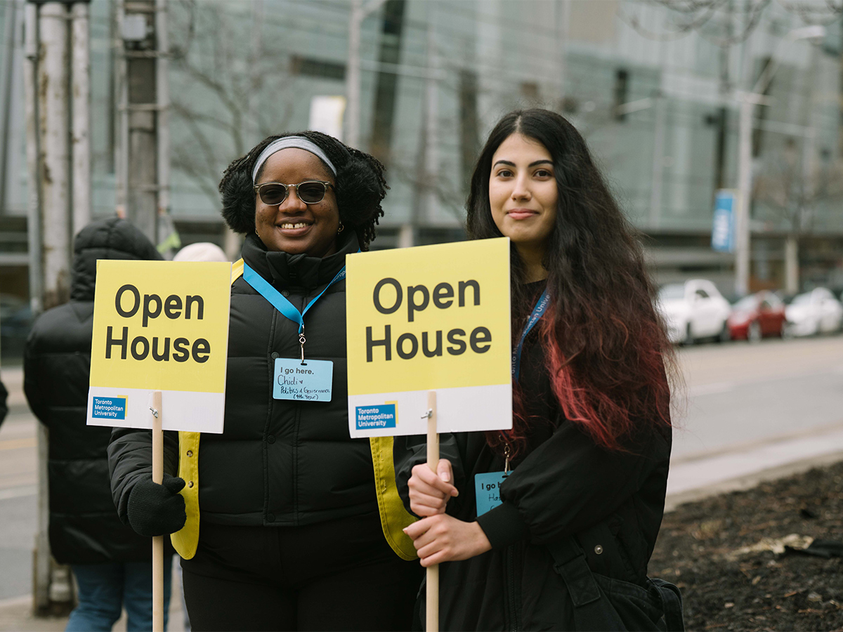 A pair of Open House tour guides with signs smile at guests along Church Street.