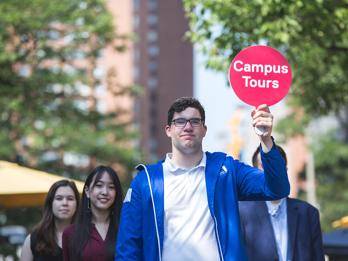 Visitors follow a student guide holding a paddle on a TMU campus tour.