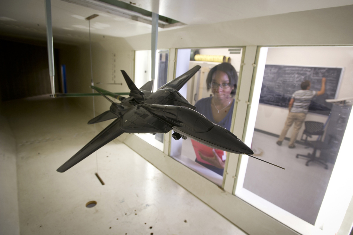 A female graduate student observes a model airplane in the wind tunnel