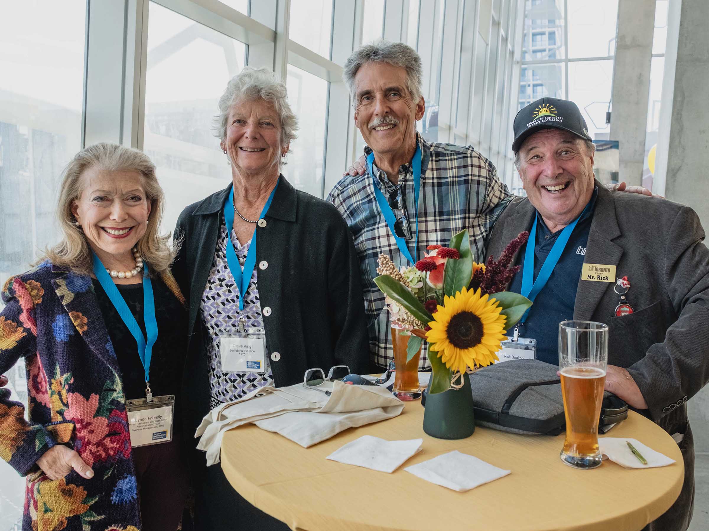 Four smiling senior alumni gathered at high top table at Alumni Reunion anniversary reception