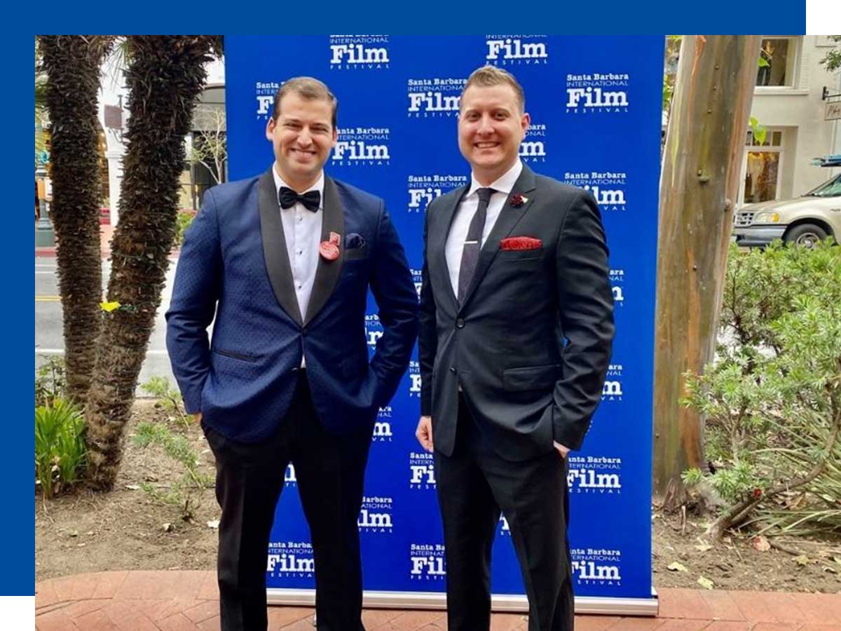 Rider and Peck stand in front of a step and repeat promoting the Santa Barbara International Film Festival dressed in suits