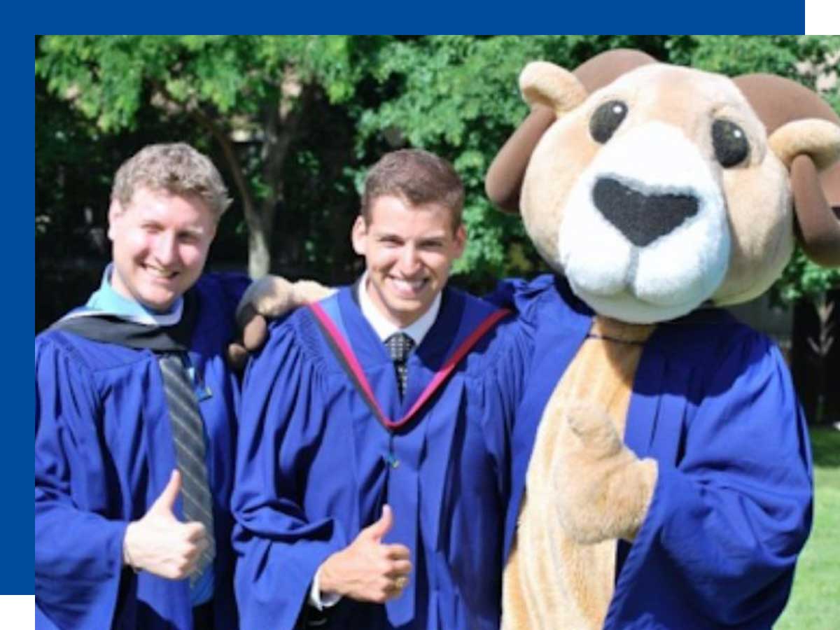 Corey Peck and Derek Rider in graduation garb posing with their thumbs up next to Ryerson Mascot Eggy