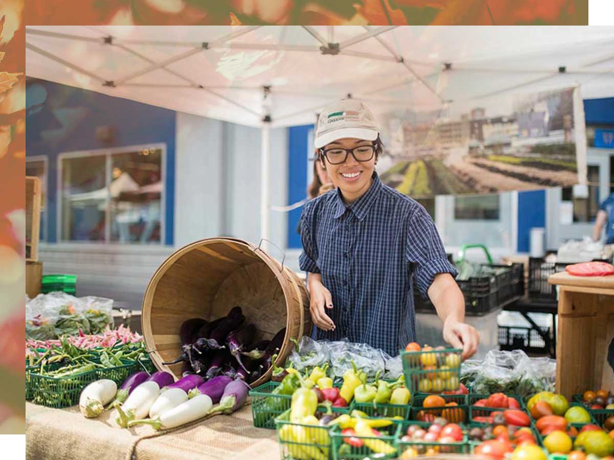 Young woman at a farmer’s market table displaying colourful vegetables