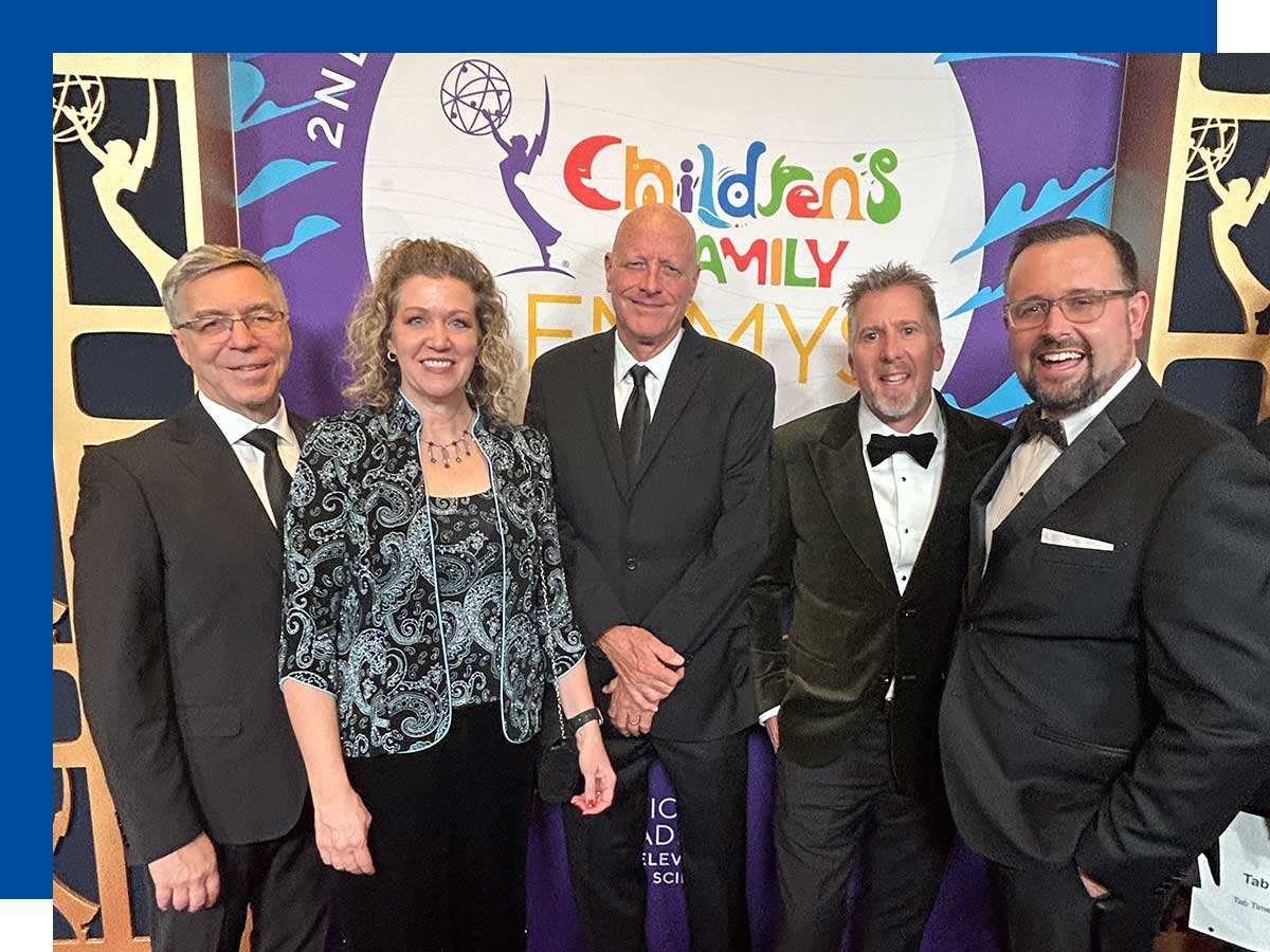  The producing team for All-Round Champions are in formal wear and stand in front of Emmy award signage.