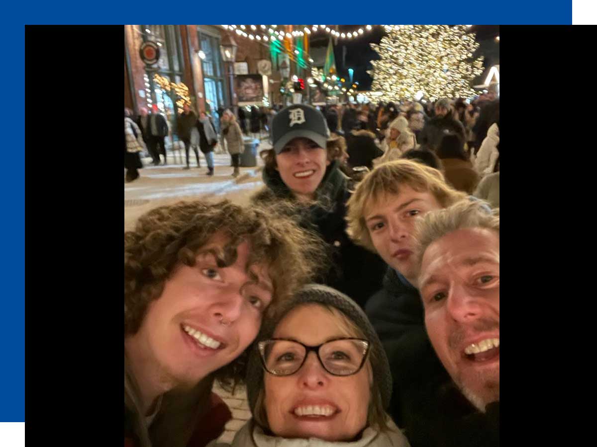  A selfie shot of the family taken outdoors, with festive holiday lights and shoppers in the background.