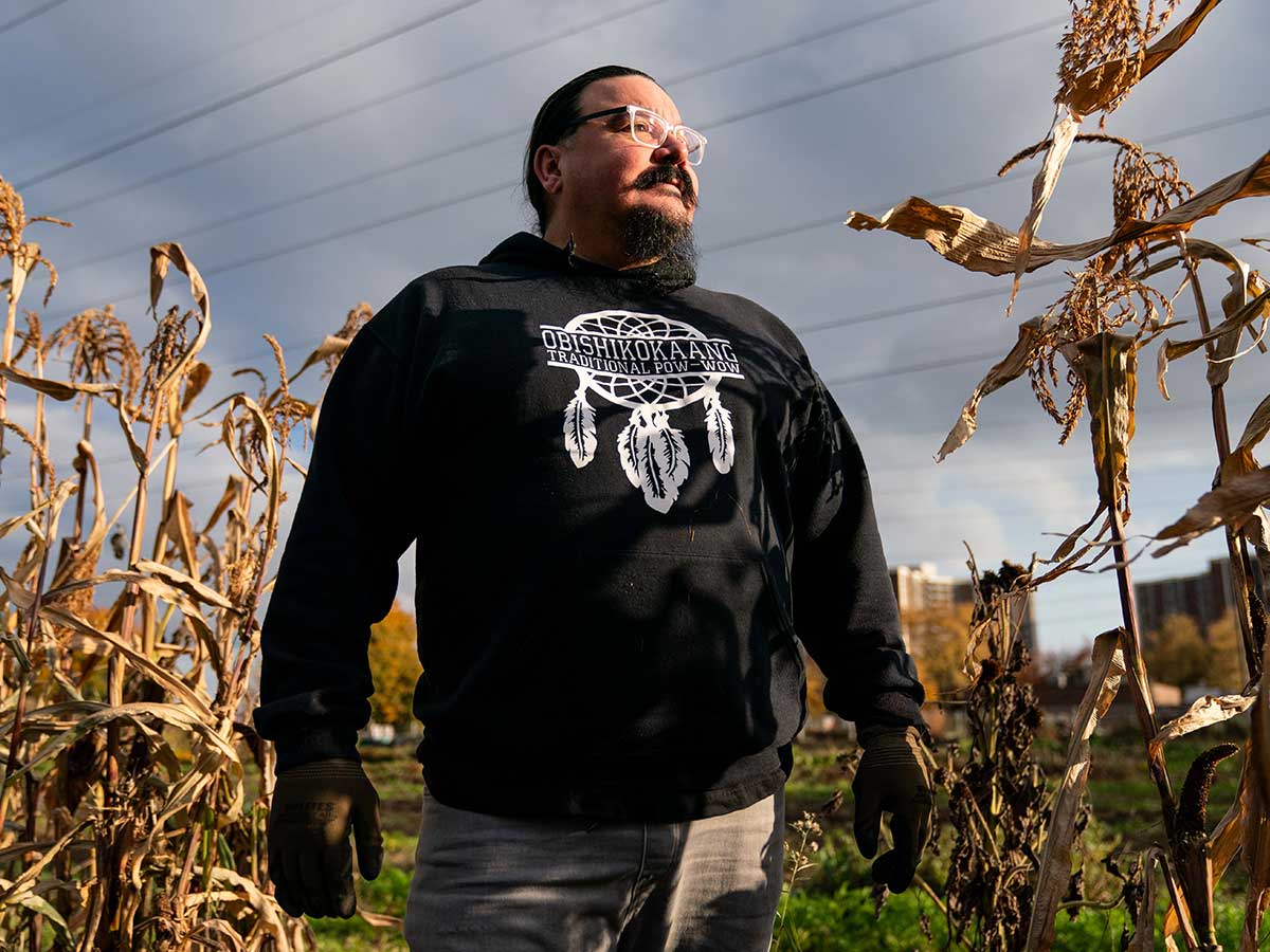 Indigenous person standing within dried corn stalks. (Indigenous Food Sovereignty for The Narwhal by Sid Naidu).