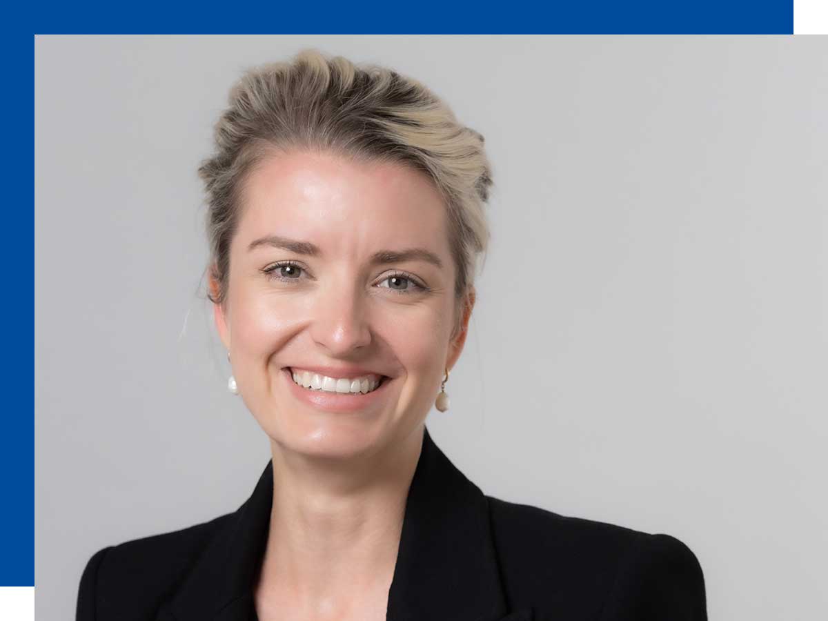 A woman stands against a white background, smiling into the camera.