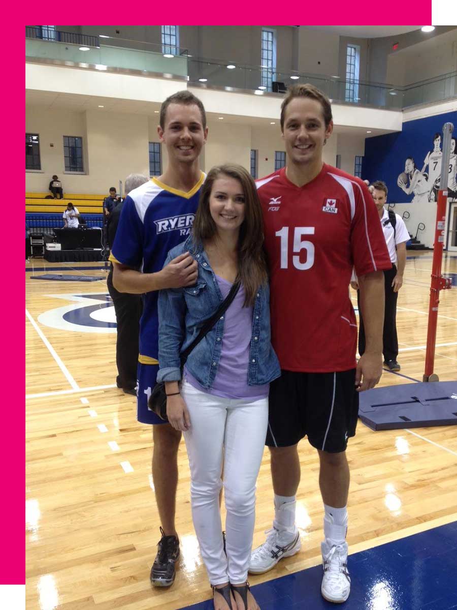 Two men wearing sports jerseys and a woman stand in a gymnasium.