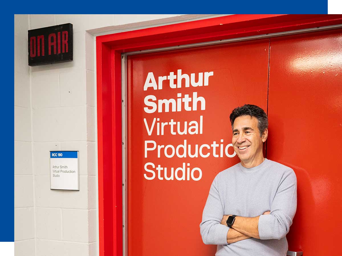 Man smiles and stands with his arms crossed in front of the double doors to the Arthur Smith Virtual Production Studio.