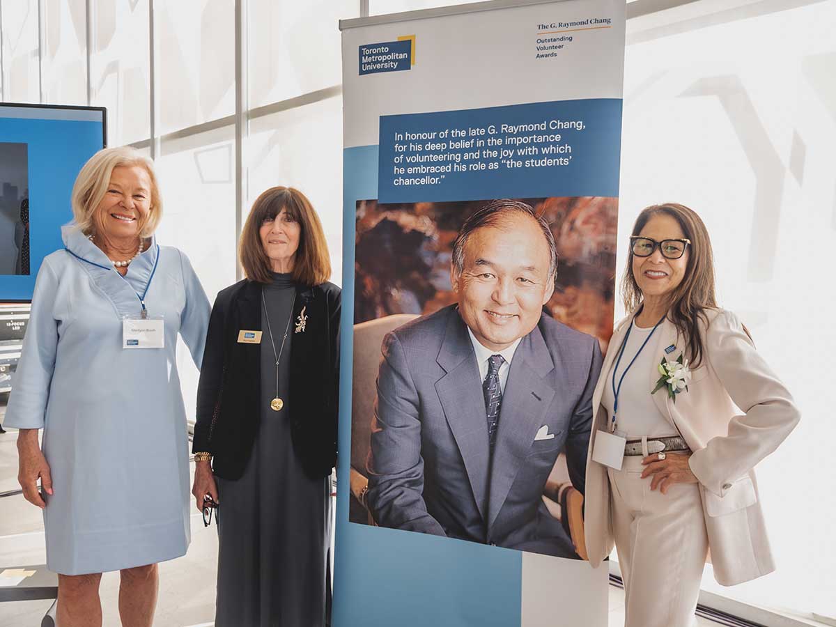 TMU leaders Marilynn Booth, Rivi Frankle and Donette Chin-Loy Chang pose beside a poster honouring G. Raymond Chang