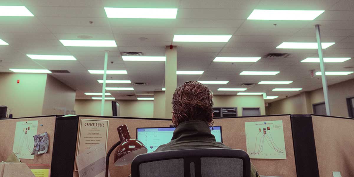 Film still looking at the back of a person working at a computer in a cubical. Image credit: Kenya-Jade Pinto