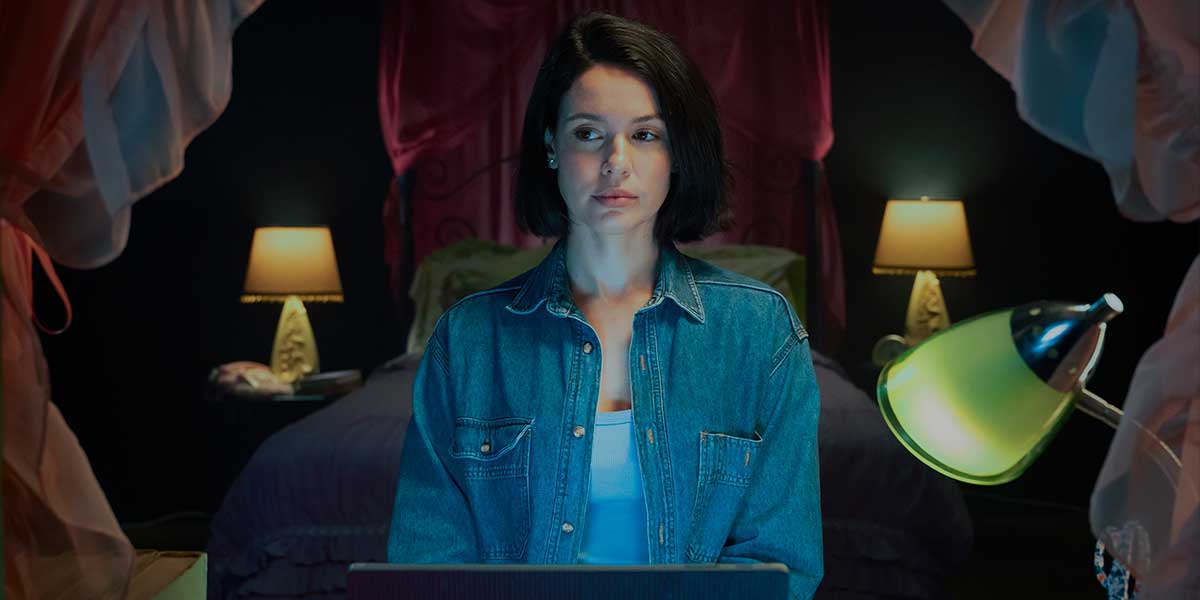 Film still of woman in a darkened bedroom with her computer