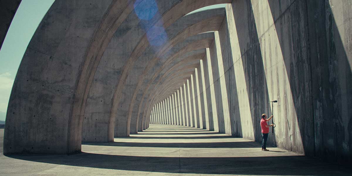 Film still of a man looking for ghosts with a microphone in an architectural feature