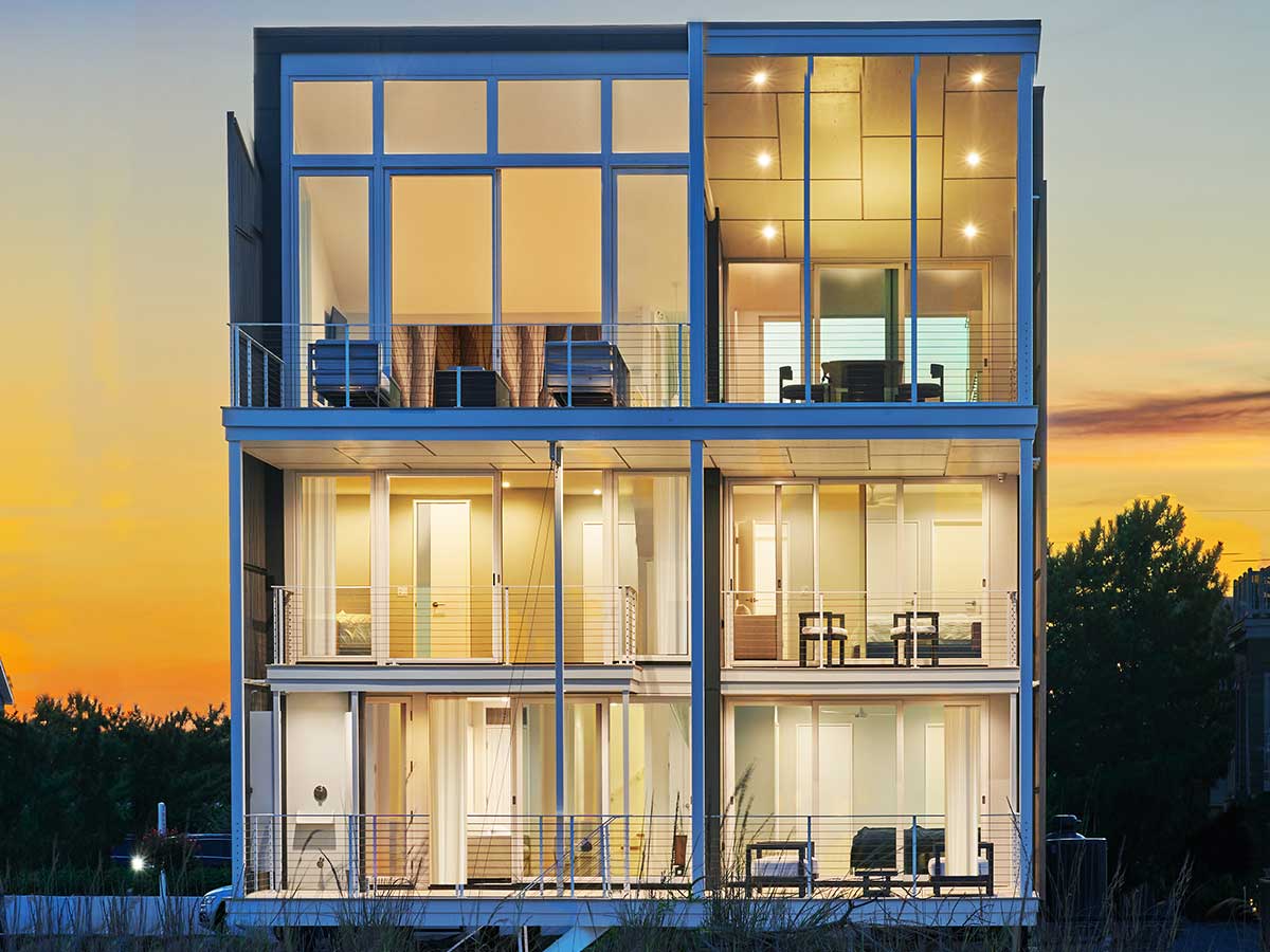 The interior of a modern home with floor to ceiling windows facing a body of water at dusk.