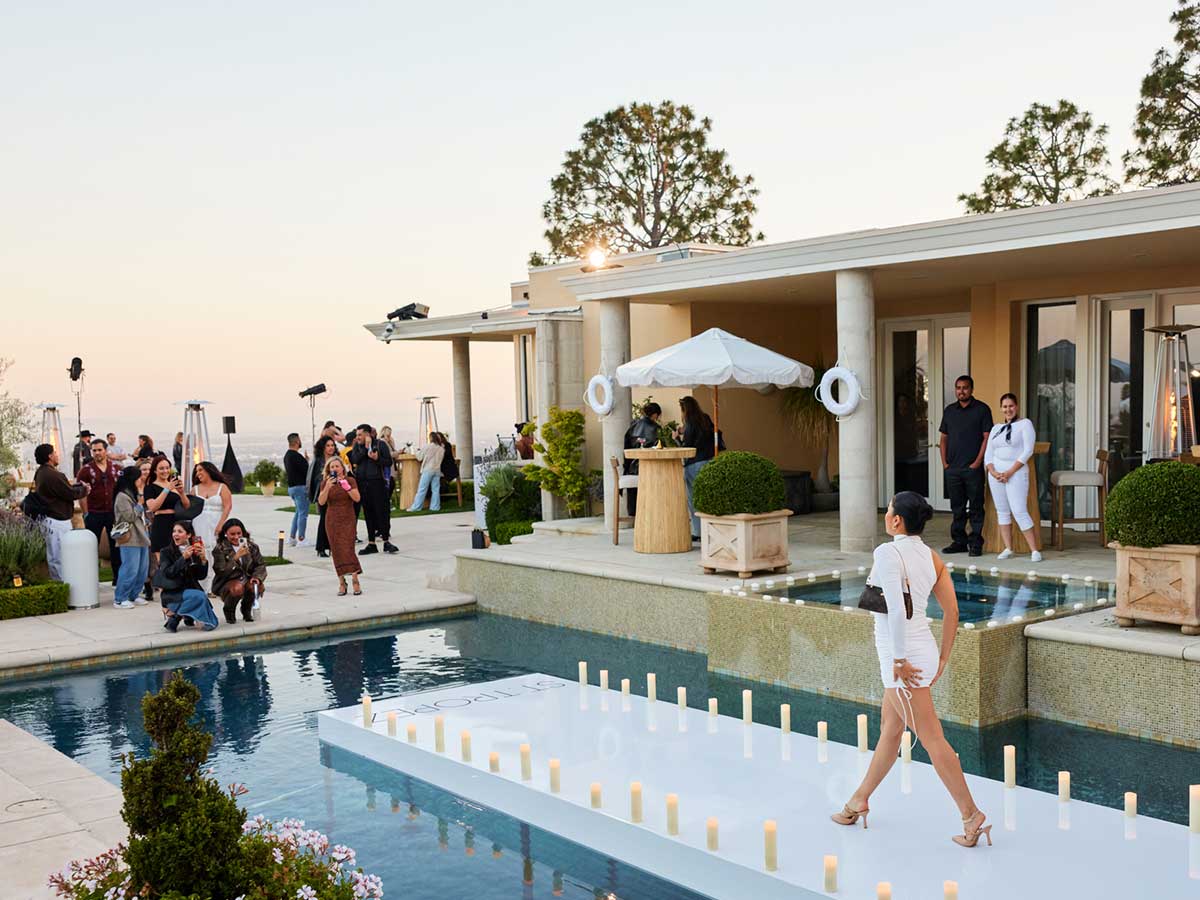 A woman walks on an aisle branded with St. Tropez in the middle of a pool as people take her photograph.