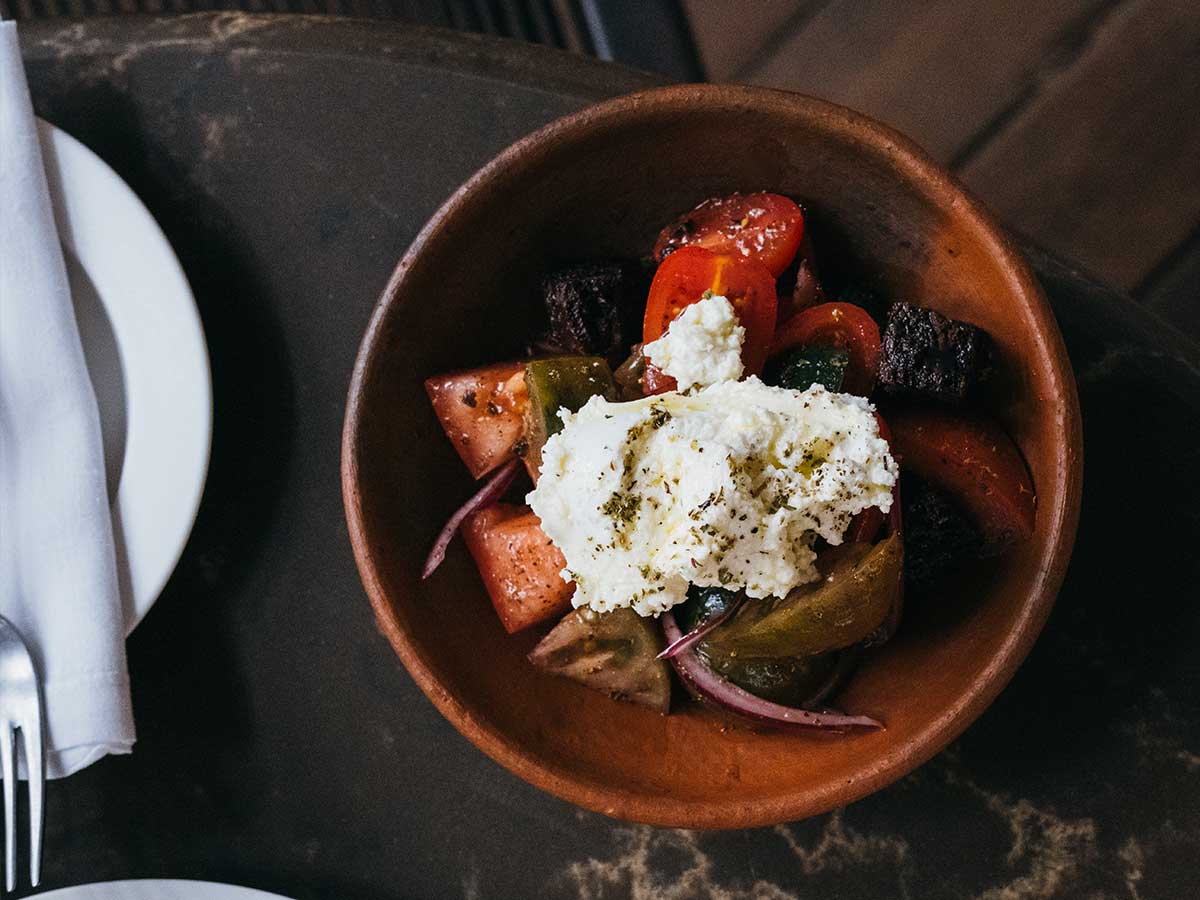 A brown bowl with a Greek salad topped with garnishing
