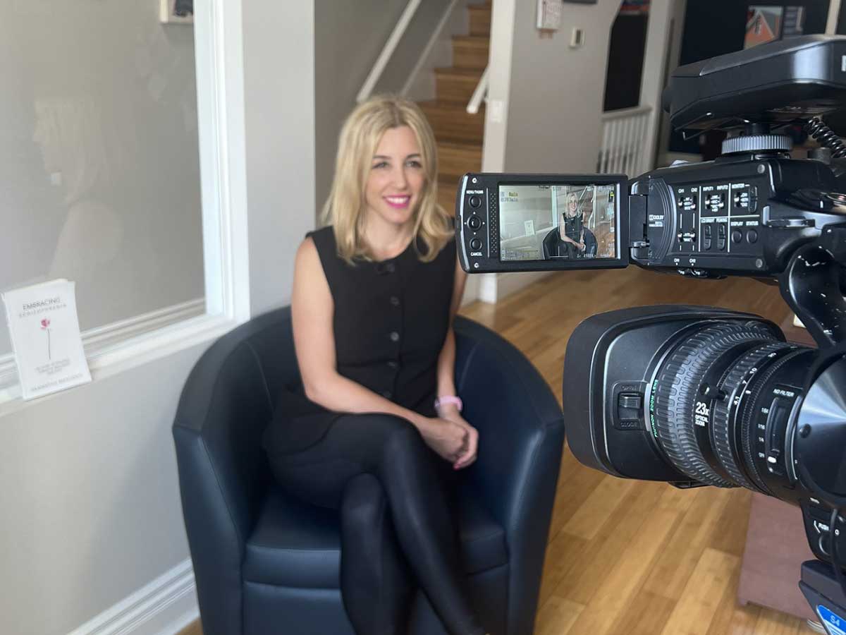 A woman sits on a chair in front of a video camera. Her image can also be seen on the video camera screen. Photo by Mindy Tweedle, Tweedle Productions Inc.