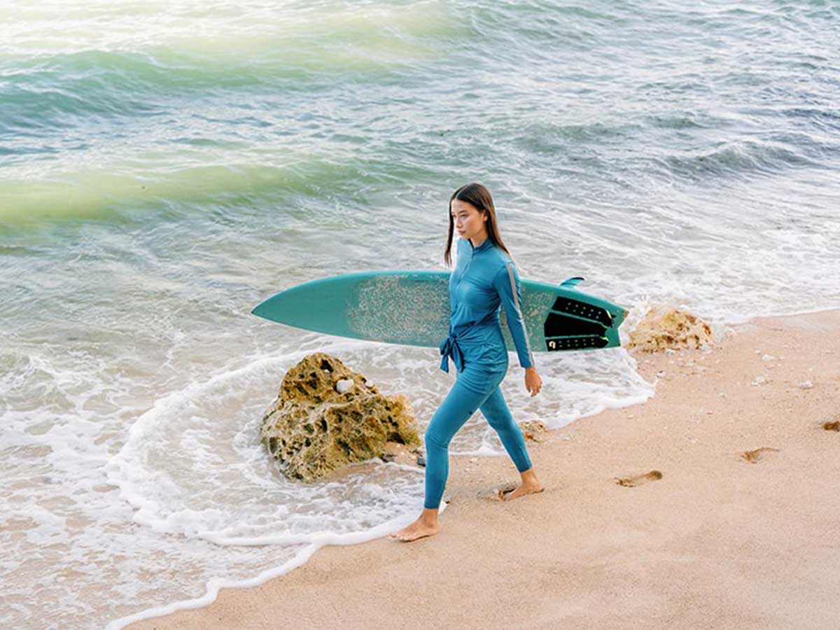 Woman wears blue swimwear and holds a surfboard at the beach.