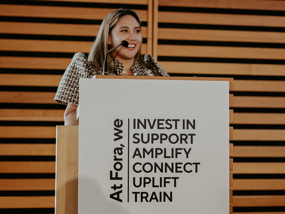 Woman stands at a podium at a Fora Network for Change event.