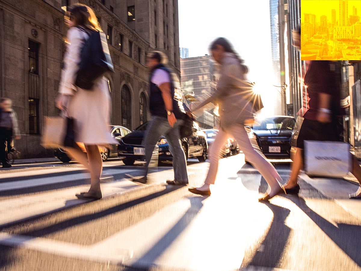 People walking across the street in a downtown setting.